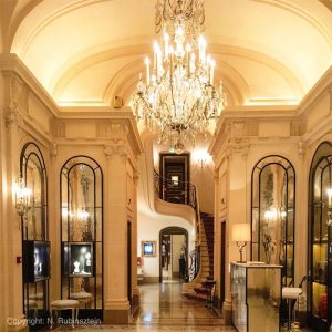 Picture of Hotel Plaza Athénée in Paris for blog "Lobby and Tea". Contains huge and stunning chandelier, shops and staircases.