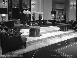 Picture of Prince de Galles Hotel in Paris. The picture features the hotel's lobby. Sofas are displayed around the room and are decorated with tiger-printed pillows. There are three huge flower bouquets with white flowers. A huge carpet lies on the ground and there are chandeliers hanging all around the place.