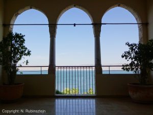 Picture of the Scots Hotel in Tiberias featuring three arches with a view on the Tiberias Lake. These three arches can be found on one of the hotel balconies which offer a table, sofa's and plants to their guests who wish to relax.
