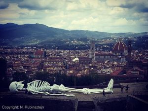 Florence, Italy featuring a huge piece of art of a skeleton which is lying on a hill with a view on Florence.
