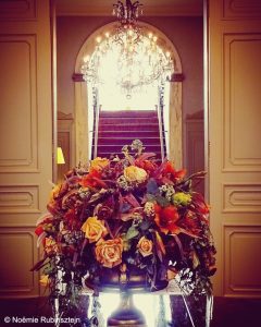 Picture of Oud Huis de Peellaert in Bruges featuring a huge flower bouquet composed of red, orange, purple, yellow and red flowers. The bouquet was placed on a table in the middle of two doors leading to the hotel's staircase and chandelier.