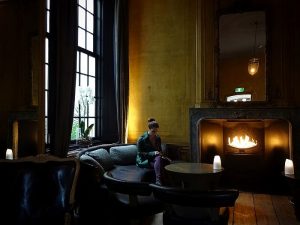 Picture of the The Dylan Hotel in Amsterdam, featuring its lobby, with huge windows, curtains, a fireplace, sofas and yellow wallpaper.