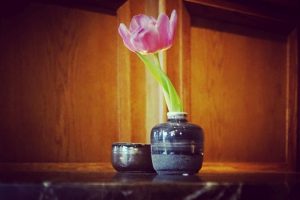 This photo was take in De Gulde Schoen hotel in Antwerp and features a pink flower in a small grey vase on a lobby table